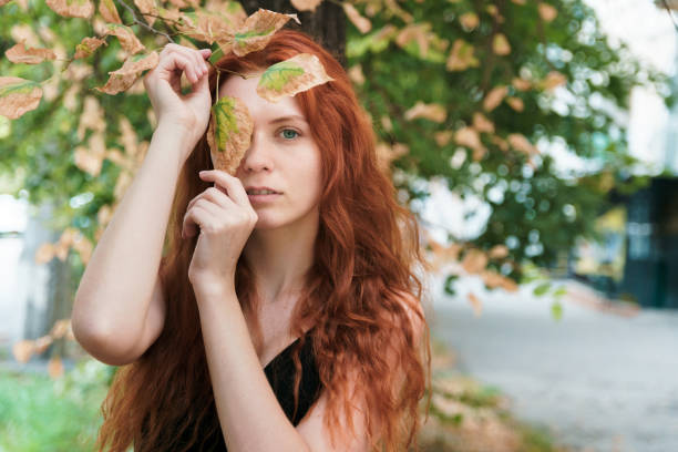 Redheaded girl with a natural look holding tree leaves.