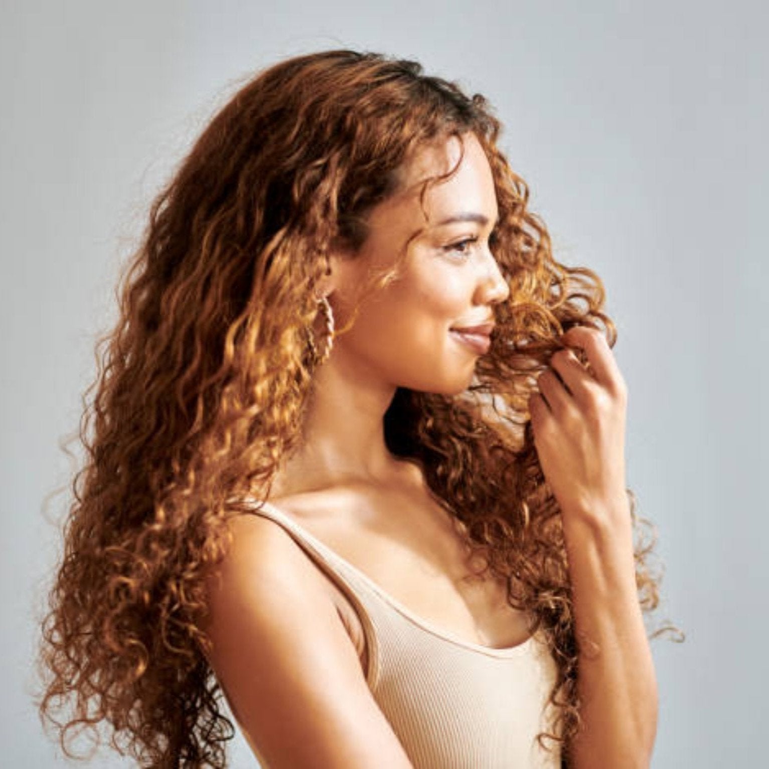 Model applying TCB Daily Curl Conditioner to her curly hair, showcasing soft, defined curls and a healthy shine.