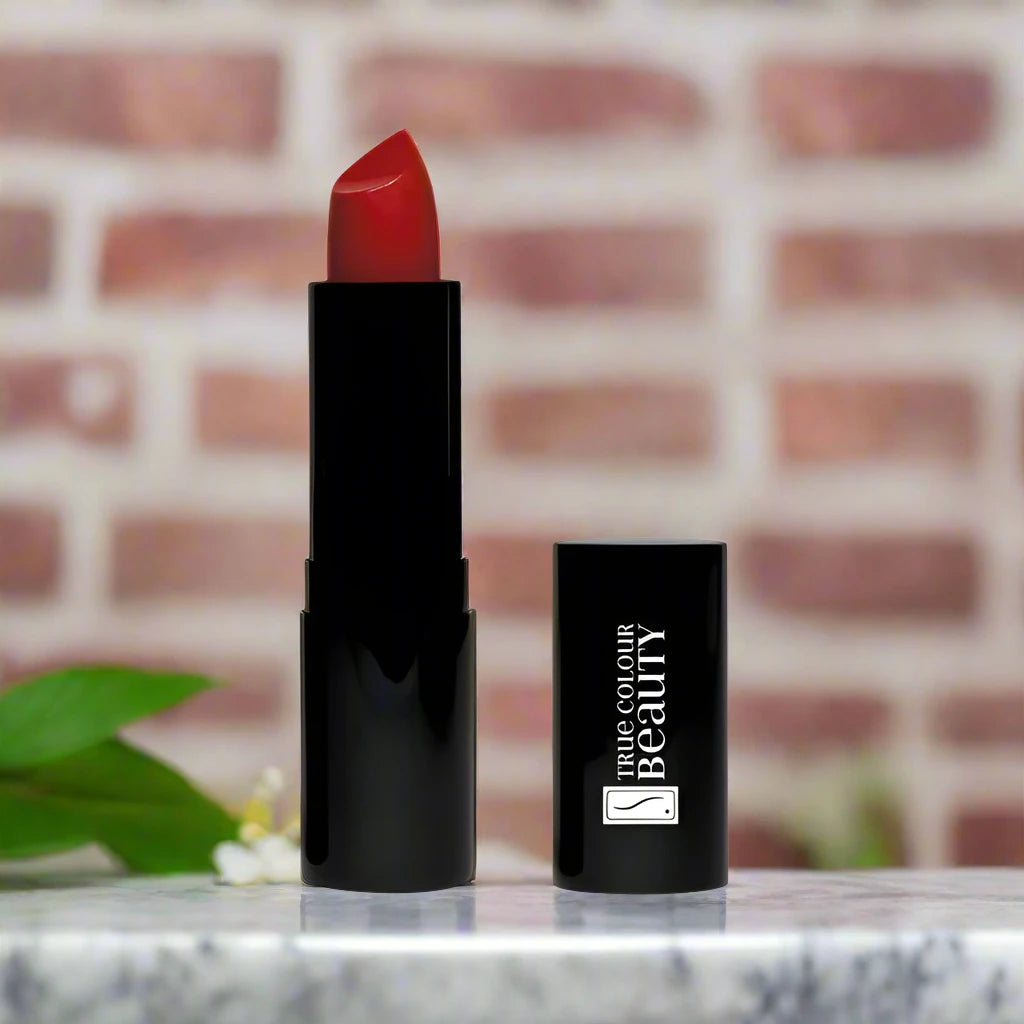 True Colour Beauty's Glamorous Red Luxury Lipstick on a marble counter-top with a red brick wall background.